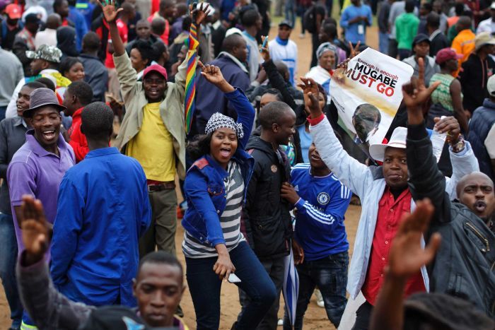 Anti-Mugabe protest in Zimbabwe A group of colourfully dressed people walk through the streets of Harare, one holds a poster saying "Mugabe must go".