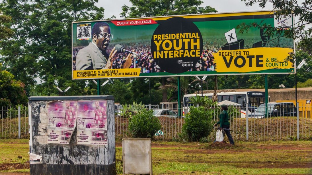 A woman in military uniform walks past a billboard for the ZANU PF in Harare