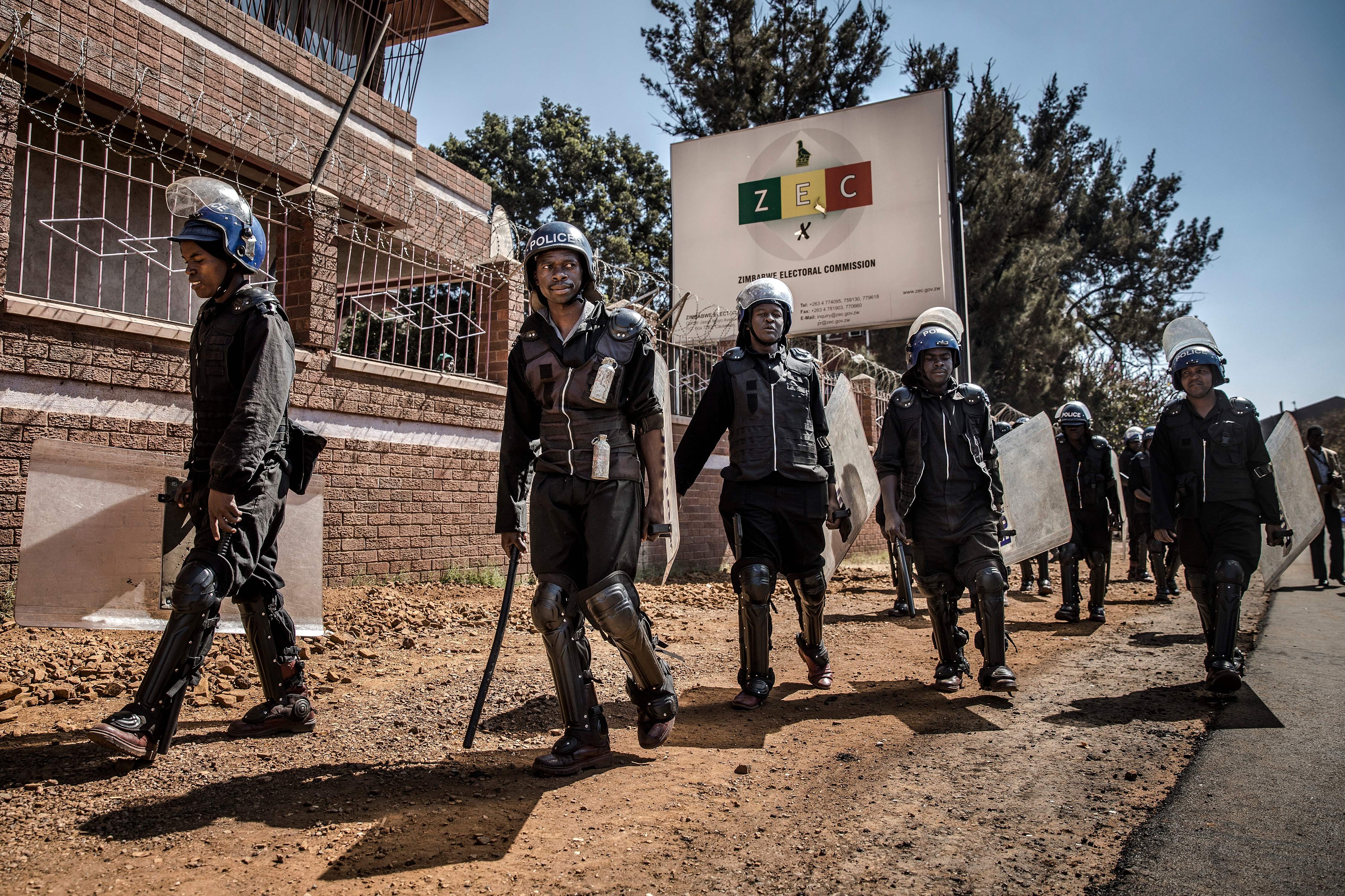 Zimbabwean anti riot police officers stand guard at the entrance of the Zimbabwe Electoral Commission (ZEC) headquarters in Harare on August 1, 2018, as supporters of the opposition party Movement for Democratic Change (MDC) protest against alleged widespread fraud by the election authority and ruling party, after the announcement of the election's results. - Zimbabwe's ruling ZANU-PF party won the most seats in parliament, official results showed on August 1, 2018, but EU observers criticised the Zimbabwe elections for being held on an "un-level playing field". (Photo by Luis TATO / AFP) (Photo credit should read LUIS TATO/AFP/Getty Images)
