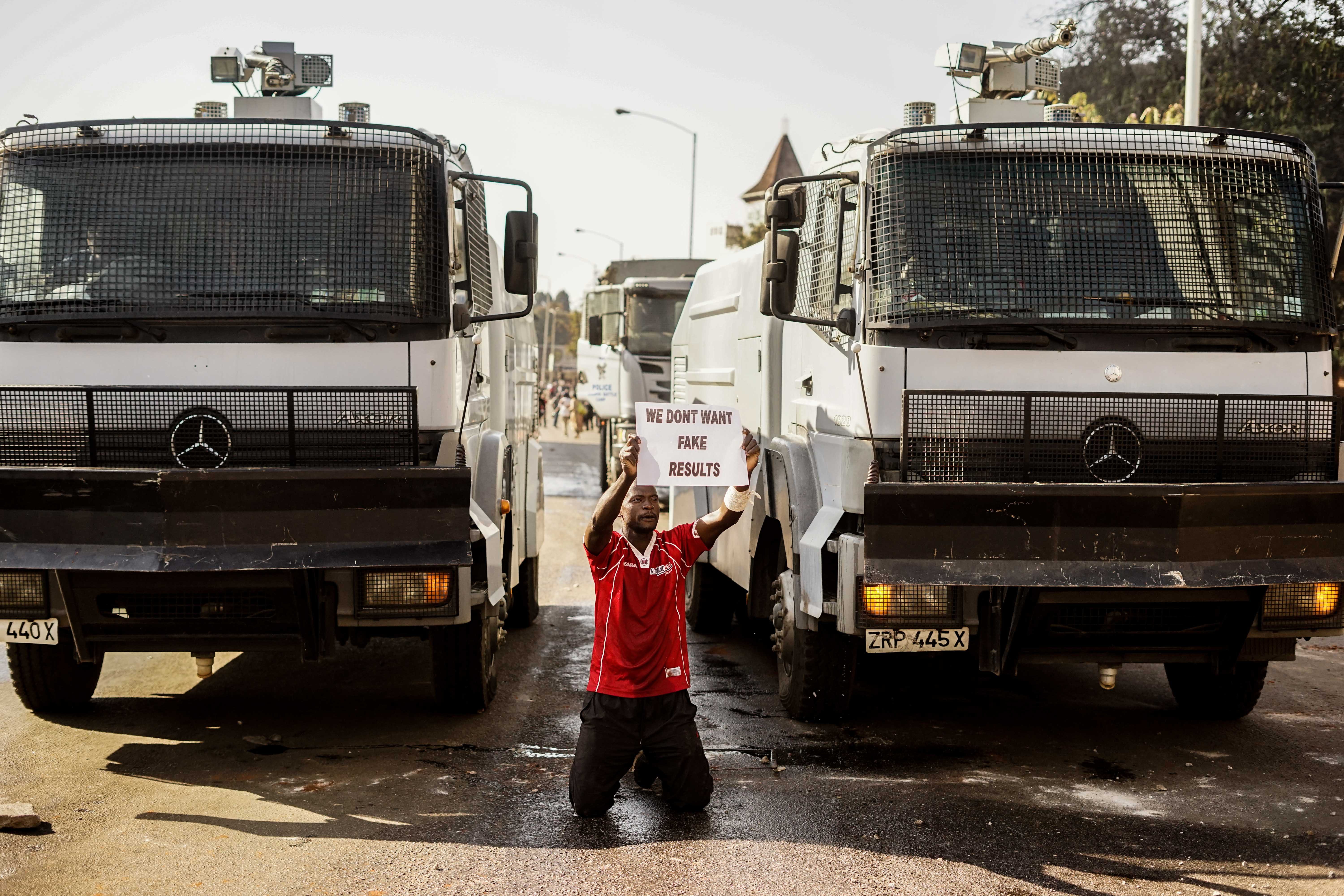 A demonstrator holds a placard as he kneels in front of police water cannons, on August 1 2018, in Harare as protests erupted over alleged fraud in the country's election. - Protests in Zimbabwe's historic elections turned bloody on August 1 as a man was shot dead during demonstrations over alleged vote fraud and the president appealed for calm. The man died after soldiers fired live ammunition during opposition protests in downtown Harare, AFP reporters saw. (Photo by Zinyange AUNTONY / AFP) (Photo credit should read ZINYANGE AUNTONY/AFP/Getty Images)