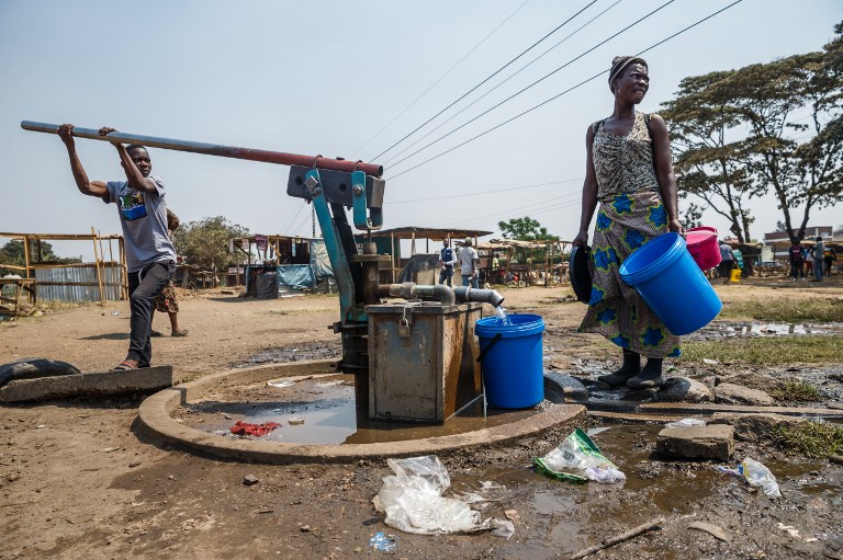 A young boy pumps water from a borehole as a woman collects water into buckets in Glen View, a suburb of Zimbabwe's capital Harare where the cholera outbreak was first detected, on September 19, 2018. 