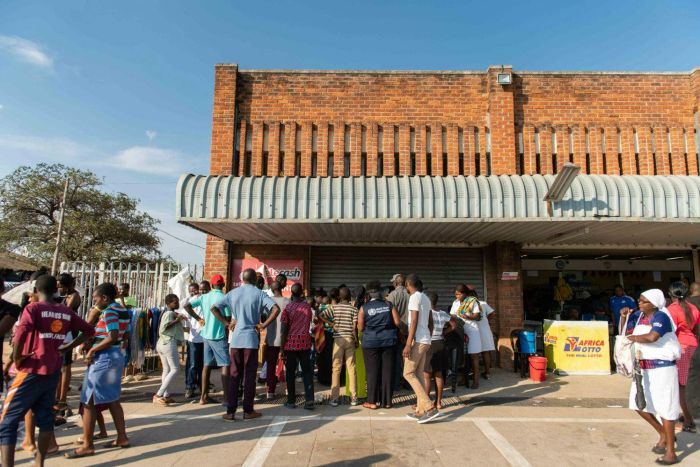 Zimbabwe cholera outbreak a group of people que outside of a brick building