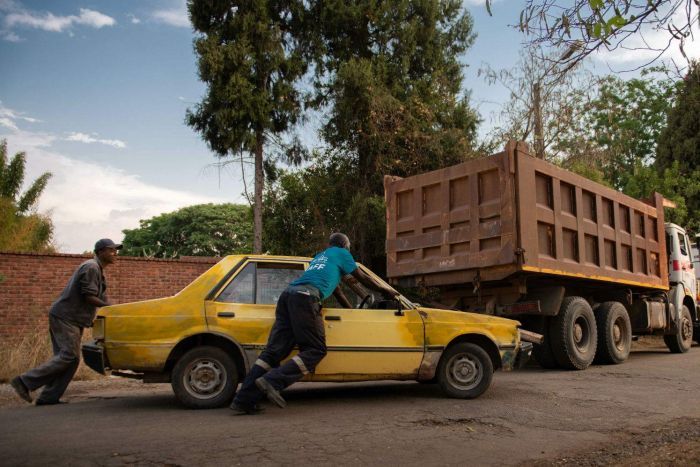Zimbabweans push a car along the road two men push a car along the road