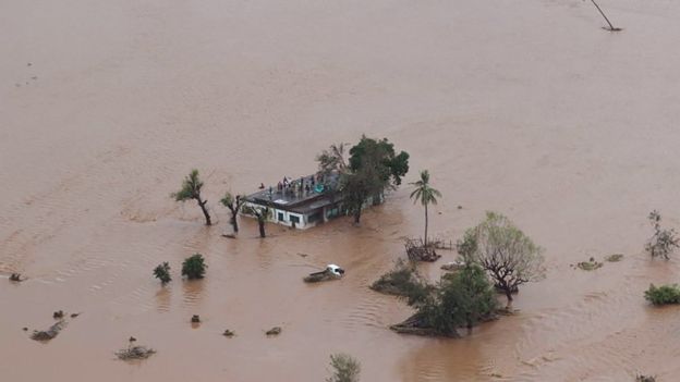 People stand on a roof of a house cut off by flood water