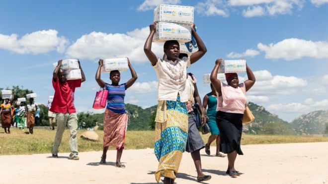 Women carry boxes of porridge for their children, on March 13, 2019, in the Mutoko rural area of Zimbabwe
