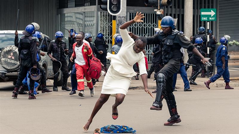 A police officer tackles a woman with his boot outside the MDC headquarters in Harare [Jekesai Njikizana/AFP] 
