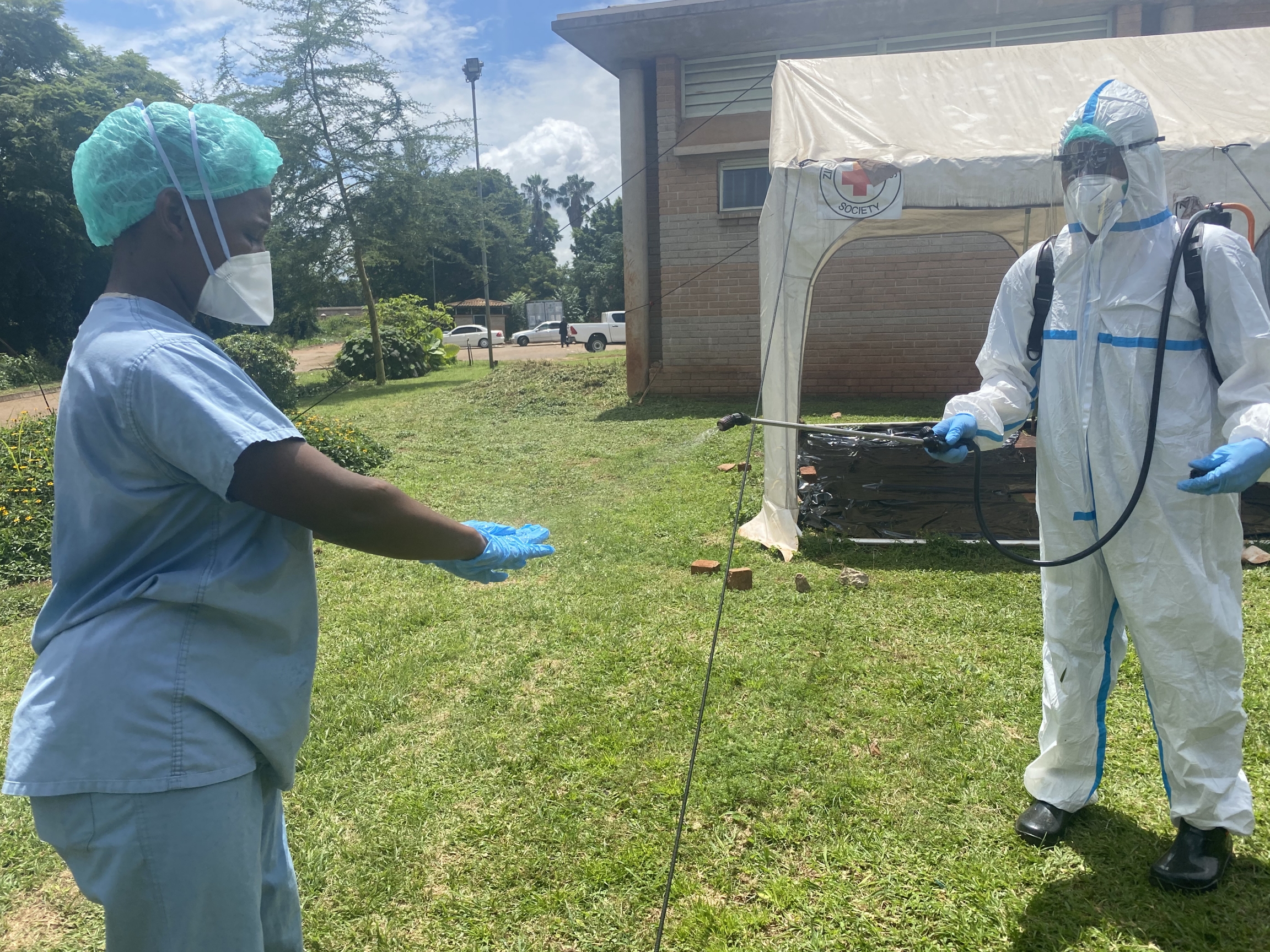 A health official disinfects a colleague, both wear protective gear. 