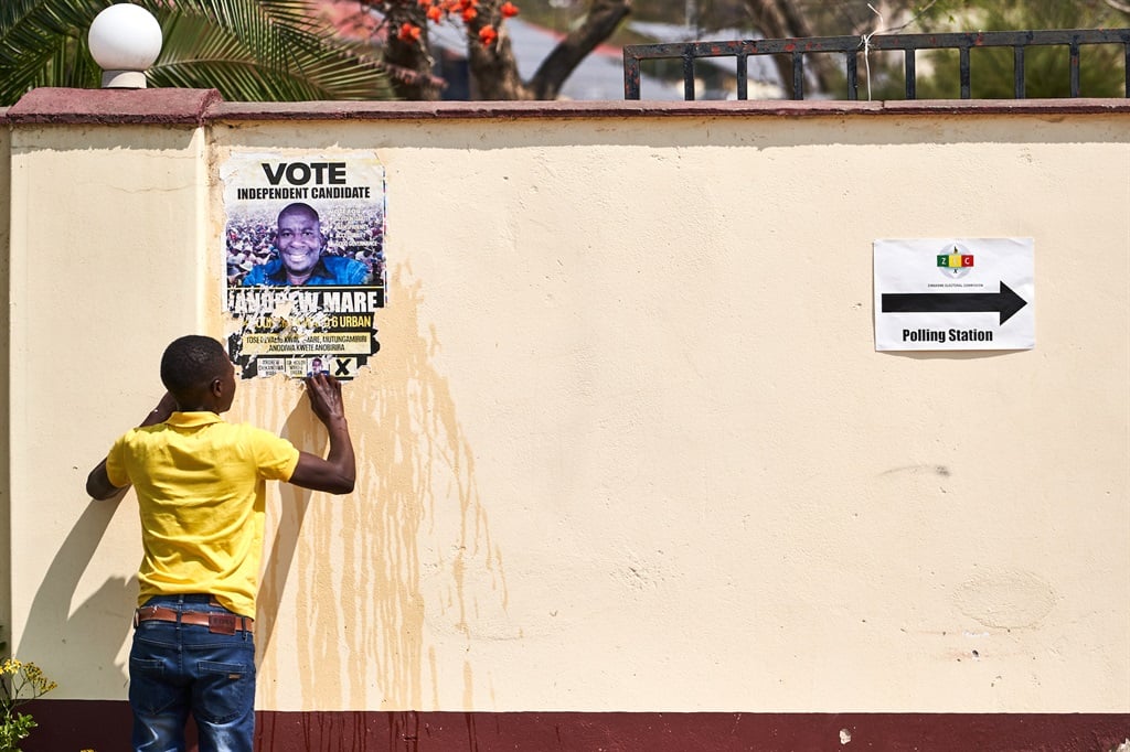 A man removes an election campaign poster next to a polling station in Zvishavane, Zimbabwe on 22 August 2023. (Photo by Zinyange AUNTONY / AFP) A man removes an election campaign poster next to