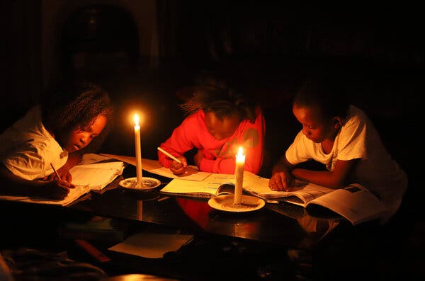 Three children huddle over books, studying by candlelight.