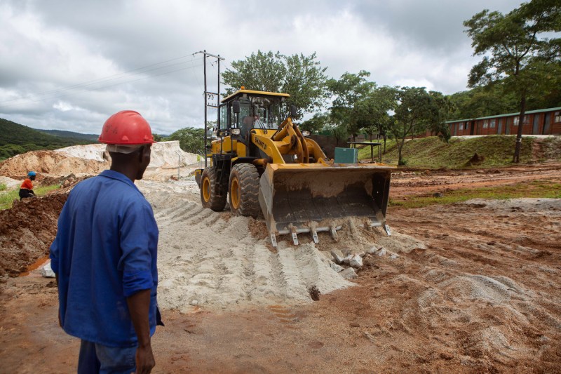 A foreman looks on as an earth mover works on the slippery road at Arcadia Mine on Jan. 11, 2022 in Goromonzi, Zimbabwe. ​