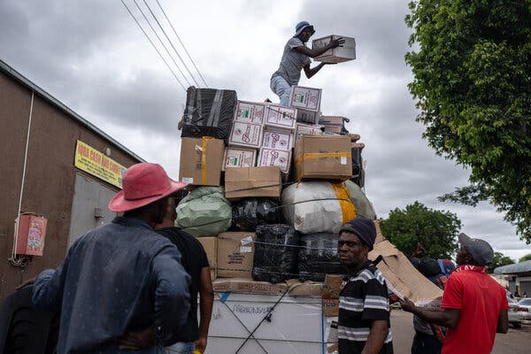 A truck is piled very high with goods in Musina, with man standing atop the pile holding a box and others stand around beside it on the ground. 