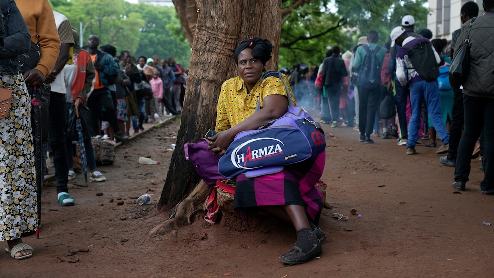 A woman takes a break from the queue outside the passport offices in Harare, Wednesday, Dec. 20, 2023. Atop many Christmas wish lists in economically troubled Zimbabwe is a travel document and people are flooding the passport office this holiday season ahead of a price hike planned in the New Year. The desperation at the office in the capital is palpable as some people fear the hike could push the cost of obtaining a passport out of reach and economic gloom feeds a surge in migration. (AP Photo/Tsvangirayi Mukwazhi)