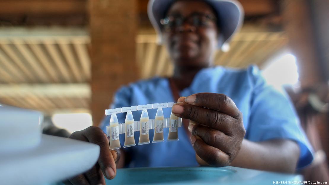 A woman, blurry in the background, holds up five little vials of cholera vaccines